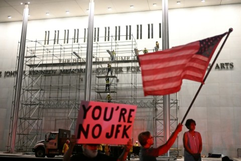 Protesters wave a US flag and hold a sign reading 'You're no JFK' as workers build scaffolding at the Kennedy Center ahead of the removal of Donald Trump's name