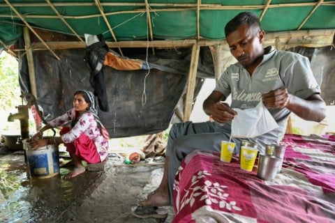 Debvati washing clothes as her husband farmer Bhole Shankar pours fruit juice after returning from work in approximately 40 degrees Celsius temperatures, inside their shanty on the Yamuna river floodplains in New Delhi