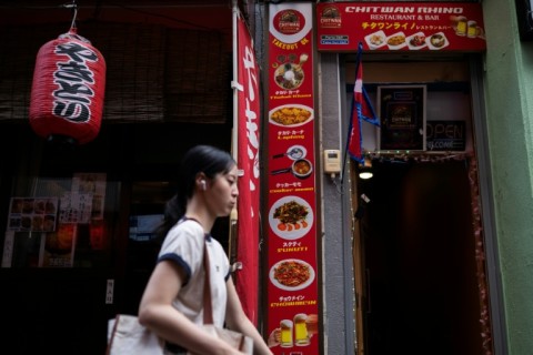 A woman passes a Japanese restaurant and the Chitwan Rhino Restaurant and Bar in the Okubo–Shin area, one stop north of Shinjuku metro