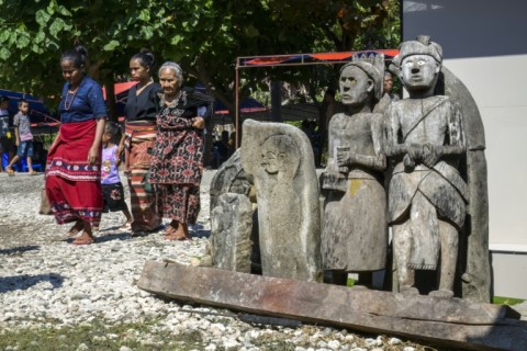 Sumbanese women wearing local ikat fabrics pass some of the statues and tombs that dot every village