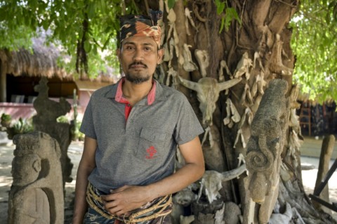 Umbu Remi Deta, a Sumba maramba (nobleman), stands in front of a tree hung with the skulls of sacrificial animals