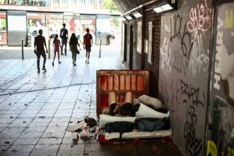People walk past a man lying on a makeshift bed in a central London underpass