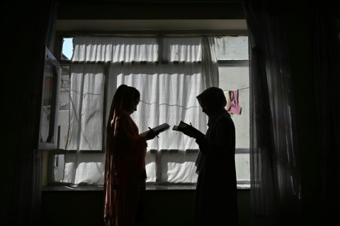 Two Afghan girls studying at home with their father