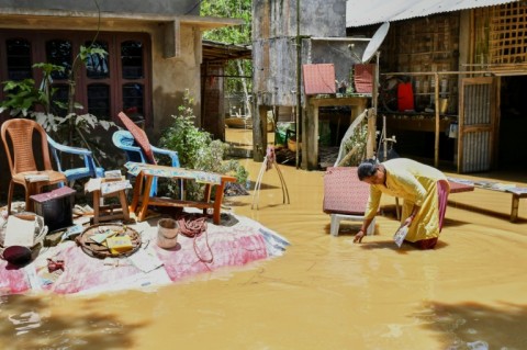 A woman salvages belongings outside her house damaged by floodwaters following heavy rains in Assam's Jorhat district on July 21, 2026