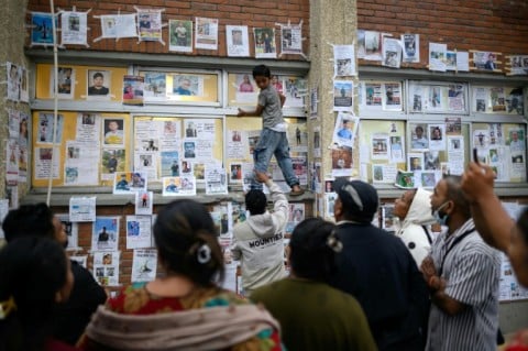 A young boy (C) climbs on a ledge to paste photographs of missing persons in the aftermath of flash floods