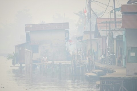 A man sits by the Kapuas river as thick smoke and haze shrouds the city of Pontianak in West Kalimantan