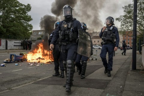 Riot police officers walk past burning trash in Toulouse