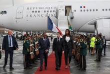 France’s President Emmanuel Macron (C) is welcomed by South African Minister of the Department of Cooperative Governance and Traditional Affairs (COGTA) Velenkosini Hlabisa (CL) upon Macron's arrival at the OR Tambo International airport in Ekurhuleni on November 21, 2025 ahead of the G20 leader's Summit. (