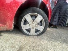 A red Chevrolet Aveo sedan, with a deflated tire.