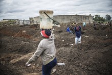 A woman balances a bucket full of soil as artisanal miners digging holes look for gold in a patch of land outside Springs, Ekurhuleni, on February 15, 2026.