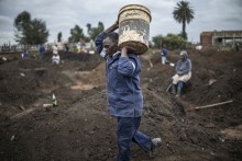 A man carries a bucket full of soil as artisanal miners digging holes look for gold in a patch of land outside Springs, Ekurhuleni, on February 15, 2026.