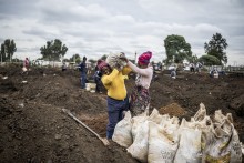 A woman grimaces as she is helped to load a sack of soil on her shoulder in a patch of land where artisanal miners look for gold outside Springs, Ekurhuleni, on February 15, 2026.