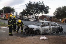 Firefighters spray water into a burning vehicle following clashes between local residents and foreign nationals in Soweto on October 8, 2026.