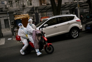 Health workers wearing protective equipment (PPE) ride a scooter near a residential area under lockdown