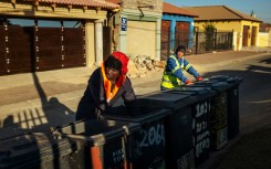 A man looks inside a trash bin in search of collectible waste while a PikitUp employee looks at him in Johannesburg, South Africa.