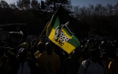 A man holds a flag of the South African ruling party African National Congress (ANC), as he gathers with supporters of former South African President Jacob Zuma outside House Hill building during the former South African president appearance at the Zondo Commission in Johannesburg, South Africa on July 15, 2019.