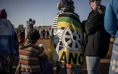 A woman wearing a blanket printed with the logo of South African ruling party African National Congress (ANC) queues with residents at a football field in the early morning during a distribution of hampers, masks, soap and sanitiser organised by different charities at the Iterileng informal settlement near Laudium, Pretoria, on May 20, 2020.