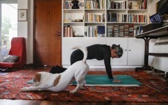 Thanks to an online pilates course, a Cypriot woman exercises at home, while her dog stretches too beside her.