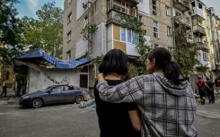 Women stand in front of a damaged residential building after shelling in the Ukrainian city of Mykolaiv, on October 1, 2022