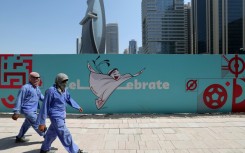 Workers walk past a billboard in Qatar showing the World Cup mascot "La'eeb"