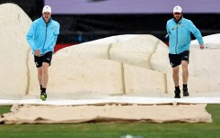 Groundsmen bring the covers on in a rainy Melbourne
