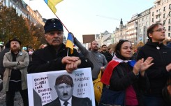 A man holds a placard reading "Occupier, thief, liar, bandit, 1968 Breznev, I'm done, 2022 Putin" depicting Russian President Vladimir Putin