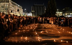People hold candles and black balloons in Athens before protests broke out at Sunday's demonstration