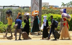 People carrying their belongings flee on foot along a street in southern Khartoum on April 18
