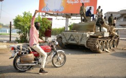 A man raises his arm in support as he drives near Sudanese army soldiers loyal to army chief Abdel Fattah al-Burhan in the Red Sea city of Port Sudan on April 20