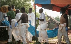 Workers carry the exhumed bodies in bodybags to the mortuary, at the mass grave site in Shakahola