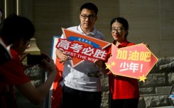 A student holds a poster reading 'Gaokao, must win' as he poses for a picture with a volunteer before entering a school in Beijing to sit an exam
