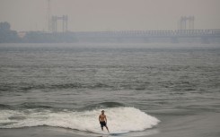 A man surfs in the St. Lawrence river with smoke caused by wildfires in northern Quebec in the background in Montreal, Canada on June 25, 2023