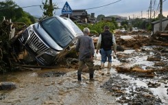 Residents walk past debris from flooding in the road in the city of Kurume, Fukuoka prefecture, on July 10, 2023