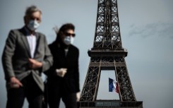 A man and a woman wearing face masks walk on Trocadero Plaza as a French national flag flies on the Eiffel Tower in Paris.