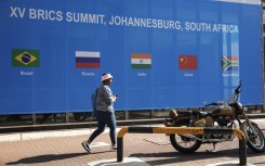 A woman walks past a banner outside the venue for the 2023 BRICS Summit at the Sandton Convention Centre in Sandton, Johannesburg, on August 20, 2023.