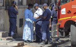 A man wearing forensic clothes speaks to a member of the SAPS at the scene of the deadly blaze in Johannesburg. AFP/Guillem Sartorio