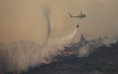 A Fire and Rescue helicopter water bombs a line of wildfire above the residential neighbourhood of Glencairn. AFP/Gianluigi Guercia
