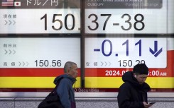 People walk past an electronic board showing the rate of the Japanese yen. AFP/Kazuhiro Nogi