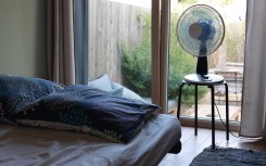 File: A fan next to a bed in a room. 