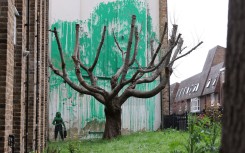 A stencil of a person having spray painted tree foliage onto a wall behind a leafless tree, a graffiti artwork confirmed as being the work of Banksy. AFP/Adrian Dennis
