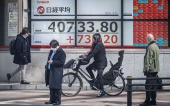 People walk past an electronic board showing a share price of the Nikkei index of the Tokyo Stock Exchange. AFP/Yuichi Yamazaki