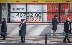 People check their phones next to an electronic board showing a share price of the Nikkei index of the Tokyo Stock Exchange in Tokyo. AFP/Yuichi Yamazaki