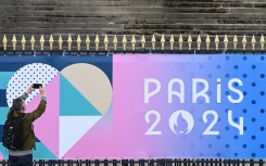 A bystander uses a smartphone to take an image of a banner for the forthcoming Paris 2024 Olympic Games. AFP/Stefano Rellandini