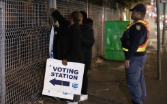 A SAPS officer looks on as an IEC officials take signs down after closing a polling station in Mowbray. AFP/Rodger Bosch