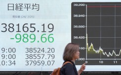 A woman walks in front of an electronic quotation board displaying the numbers of share prices on the Tokyo Stock Exchange. AFP/Kazuhiro Nogi