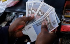 A cashier in a leading supermarket dispenses a $10 ZiG note from a till. AFP/Jekesai Njikizana