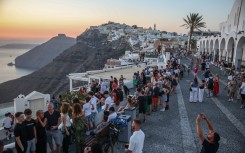 Tourists take pictures of the sunset in the village of Fira on the Greek island of Santorini. AFP/Aris Oikonomou