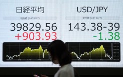 A pedestrian walks past an electronic board showing the closing numbers on the Tokyo Stock Exchange. AFP/JiJi Press