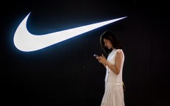 File: A woman browses her phone while walking past a Nike logo inside a shopping mall in Beijing. AFP/Nicolas Asfouri