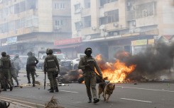 Anti-riot police officers with their dogs walk down Eduardo Mondlane Avenue past burning barricades made by protesters in Maputo. AFP/Alfredo Zuniga